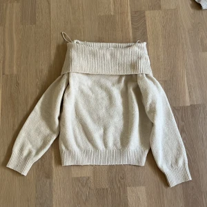 Beige offshoulder stickad tröja H&M - Säljer en beige stickad tröja från H&M med bred ribbad krage som kan bäras offshoulder. Tröjan har långa ärmar och ribbade muddar vid ärmslut och nederkant. Perfekt för dig som gillar en chill och snygg stil.