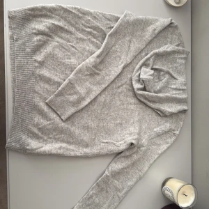 Ljusgrå tunn  hoodie i kashmir Soft Goat -  ljusgrå hoodie från Soft Goat i 100% kashmir. Tröjan har lång ärm, ribbade muddar. Perfekt för dig som gillar comfy men ändå vill se snygg ut.