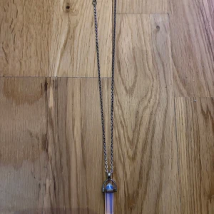 Halsband med kristallhänge i silver - Snyggt halsband med en tunn silverfärgad kedja och ett hänge i form av en spetsig kristall. Kristallen har en skimrande vit och blå ton som ger ett magiskt intryck. Perfekt för dig som gillar unika smycken med lite mystisk vibe.