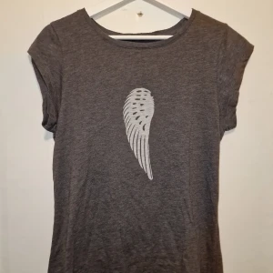Grå t-shirt Coster Copenhagen - Snygg grå t-shirt från Coast Copenhagen. Framsidan har ett coolt tryck med en vit vinge. See-through vid vingen. Dyr vid inköp. Passar mig som har S.