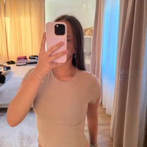 Beige ribbad t-shirt i bomull - Säljer en beige ribbad t-shirt med rund hals och korta ärmar. Modellen är figurnära och har en enkel, stilren design som passar perfekt till jeans eller kjol. Materialet är mjukt och stretchigt bomull för skön komfort hela dagen.