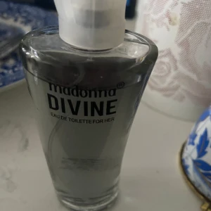 Madonna Divine Eau de Toilette - Fräsch och feminin parfym från Madonna, Divine Eau de Toilette for Her. Flaskan är transparent med en stilren, konformad design och vit spraykork. Perfekt för dig som gillar eleganta och klassiska dofter.