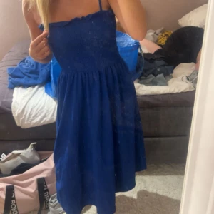 Mörkblå klänning med smock - Säljer en mörkblå klänning med smock upptill och tunna axelband. Klänningen har en mjuk, flowy passform och är knälång. Materialet känns lätt och bekvämt mot huden. 
