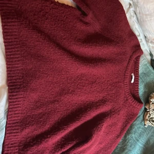 Vinröd stickad tröja med rund hals - Mysig vinröd stickad tröja med rund hals och långa ärmar. Tröjan har en enkel design med ribbade muddar vid hals, ärmslut och nederkant. Perfekt för dig som gillar en chill och klassisk look under kyliga dagar.