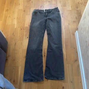 Bootcut jeans från Gina Tricot - Snygga mörkgrå bootcut jeans från Gina Tricot i storlek 170. Jeansen har klassisk femficksdesign, vita knappar och breda ben med lätt utsvängd form. Materialet är slitstarkt denim och bakfickorna har lock med knapp. Perfekta för dig som gillar retrovibbar.
