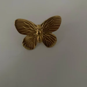 Guldfärgad ring med fjäril - Cool ring i guldfärg formad som en fjäril med detaljerade linjer på vingarna. Perfekt statement piece för dig som vill sticka ut och addera lite extra till din look. Fjärilen är stor och syns verkligen, passar dig som gillar unika accessoarer.