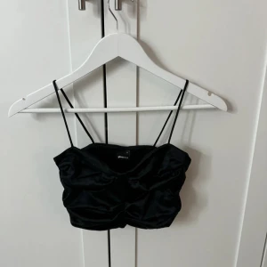 Svart satin bandeau från Gina Tricot - Supersnygg svart bandeau topp från Gina Tricot i glansigt satinmaterial. Toppen har smala axelband och en lätt rynkad effekt framtill. Nypris 350kr