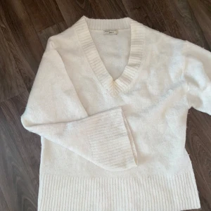 Vit stickad v-ringad tröja från Gina  - Mysig vit stickad tröja från Gina med bred ribbad kant vid ärmslut och nederkant. V-ringad hals och långärmad modell, perfekt för lager-på-lager. Mjuk och skön känsla, passar dig som gillar clean och enkel stil. Liiite nopprig men inget man lägger märke till.
