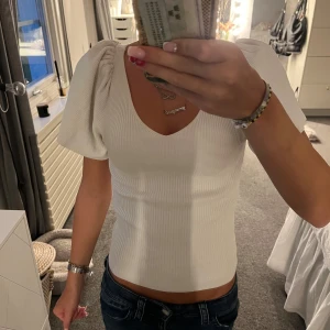 Vit ribbad topp med puffärm från ONLY - Supersnygg vit ribbad topp från ONLY i storlek XS. Toppen har korta puffärmar och v-ringning som ger en trendig look. Materialet är stretchigt och sitter snyggt på kroppen. Perfekt att styla med jeans eller kjol för en fräsch outfit.
