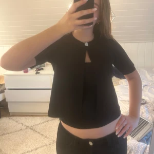 Svart kort kofta med en knapp från Gina Tricot  - Snygg svart kofta med korta ärmar och en cool öppning framtill som stängs med en silverfärgad knapp. Toppen är croppad och har en enkel, stilren look. Den är lite använd så i mycket fint skick! Hör av er vid frågor. Priset är inte hugget i sten!💗
