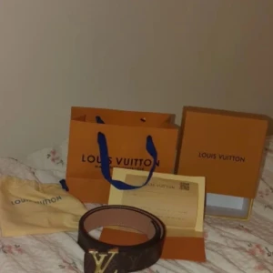 ÄKTA Brunt monogram-bälte, 110 cm, med guldfärgat spänne  - Har ett superfint bälte i brun monogram med guldfärgad logga/spänne. Det är helt oanvänt, storlek 110 cm och självklart äkta. Kommer med påse, box och kvitto (syns på bilderna).  Ett tidlöst bälte som lyfter vilken outfit som helst – både vardag och fest. Säljer det för 299 kr, så det här är verkligen ett kap 🙌 Först till kvarn!