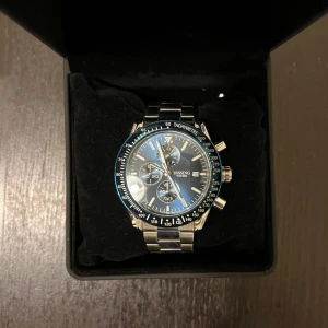 Dissing kronograf herrklocka blå/silver - Stilren kronograf från Dissing med blå urtavla, silverfärgade detaljer och datumvisning. Klockan har robust länkarmband i metall och flera små urtavlor för extra funktioner. Kommer i original ask. Perfekt accessoar för dig som gillar sportig och modern stil.