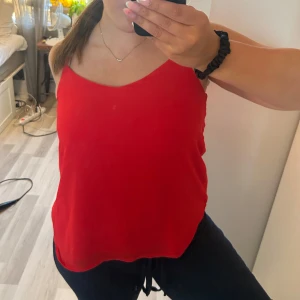 Röd linnetopp med smala axelband - Snygg röd linnetopp med smala axelband och v-ringad fram med cool detalj i ryggen. Toppen är lätt och luftig, perfekt för varma dagar. Materialet känns mjukt mot huden och har en lätt transparent look. Passar dig som gillar enkel och stilren vibe.