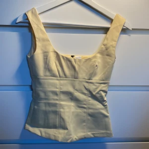 Ljusgul Zara topp - Snygg ljusgul korsett-topp från H&M i storlek XS. Toppen har breda axelband och en figurnära passform med markerade sömmar framtill som ger en cool siluett. Perfekt att styla med jeans eller kjol för en trendig look.