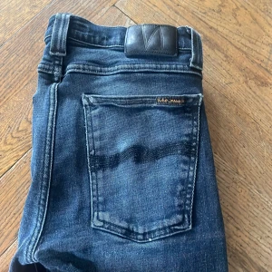 Mörkblå jeans från Nudie Jeans - Snygga mörkblå jeans från Nudie Jeans med en klassisk femficksdesign. De har en slim passform och är tillverkade i slitstarkt denim. Perfekta för en stilren look. Hål i fickorna men annars top skick , förekommer det fler frågor är det bara o hojta till🙌✌️MVH Maurice
