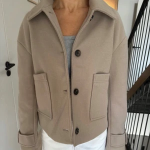 Beige kappa - Snygg beige kort kappa från Nelly. Är lite nopprig på ärmarna (se sista bilden), men annars i bra skick
