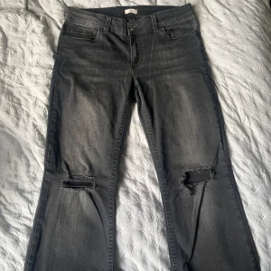 Grå bootcut jeans från Nelly - Snygga grå jeans från Nelly med bootcut passform och slitna hål på knäna. Jeansen har klassisk femficksdesign, dragkedja och knapp framtill. 
