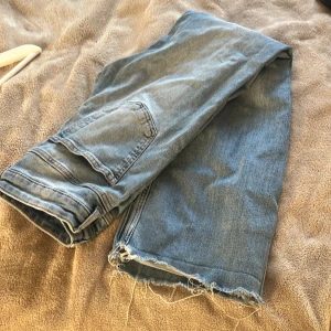 Blå jeans med rå kant - Säljer ett par ljusblå jeans med fransig, rå kant nedtill för en cool och avslappnad vibe. Klassisk femficksmodell med raka ben och normal passform. Perfekt för dig som gillar en lite edgy stil.