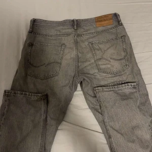 Grå loose jeans från Jack & Jones - Säljer ett par grå jeans från Jack & Jones i modellen Loose/Chris. De har en loose passform, raka ben och klassiska fem fickor. Jeansen är tillverkade i denim och har en cool, lite tvättad look. Perfekt för dig som gillar avslappnad stil.