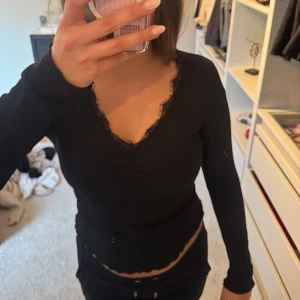 Svart långärmad topp med spets - Svart långärmad topp med spetsdetaljer längs halsringningen och ärmarna. 