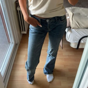 Blå bootcut jeans med broderade fickor - Säljer ett par klassiska blå jeans med bootcut passform och snygga broderade detaljer på bakfickorna. Jeansen har normal midja, fem fickor och stängs med knapp och dragkedja. Perfekta till sneakers eller boots för en chill look.