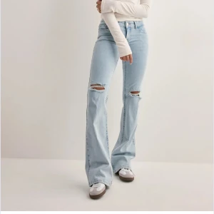 Bootcut ljusblå jeans med slitningar - Snygga ljusblå bootcut jeans med slitna hål på knäna och broderade detaljer på bakfickorna. Jeansen har låg midja och klassisk femficksdesign. Perfekta för dig som gillar en avslappnad och trendig look.