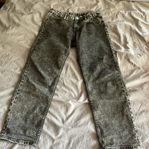 Grå tvättade jeans från H&M - Säljer ett par gråsvarta jeans från H&M med relaxed fit och tapered leg. Jeansen har justerbar midja, klassiska fem fickor och coolt tvättad look. Perfekta för dig som gillar en avslappnad stil med lite edge. Storlek 158