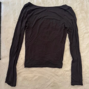 Mörkgrå långärmad topp Gina Tricot - Mörkgrå långärmad topp från Gina Tricot i storlek L. Modellen har en djup, rundad rygg och är figurnära med stretchigt material. Perfekt att styla med jeans eller kjol för en clean look. Tunn och mjuk bomullskänsla, enkel och stilren design.