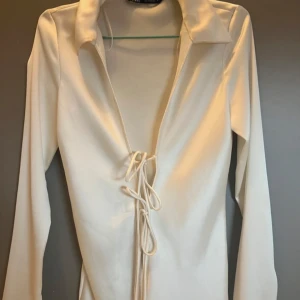 Vit skjorta med snörning - Säljer en vit skjorta från Zara med långa ärmar och snygg snörning framtill. Skjortan har en bred krage och är gjord i mjukt material som sitter skönt på kroppen. Perfekt för dig som gillar stilrena och trendiga plagg.
