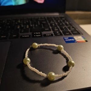 Pärlarmband med gröna och vita pärlor - Snyggt armband med små vita pärlor och fem större ljusgröna pärlor som ger en fräsch och trendig look. Perfekt att matcha med andra smycken eller bära som ett statement piece. Elastiskt band gör det enkelt att ta på och av.