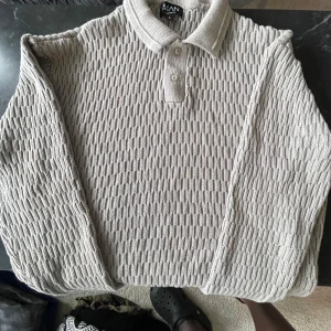 Beige stickad pikétröja från MAN - Säljer en beige stickad pikétröja från MAN med snyggt strukturerat mönster och klassisk krage. Tröjan har lång ärm och knappar vid halsen. Perfekt för dig som gillar en chill och stilren look.