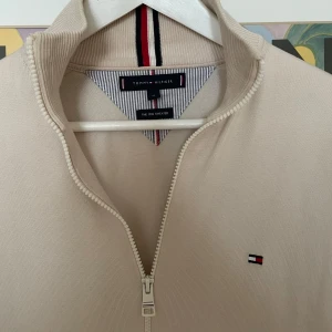 ziptröja Tommy Hilfiger - Snygg beige ziptröja från Tommy Hilfiger med diskret logga på bröstet. Tröjan har hel dragkedja, ståkrage och är tillverkad i mjuk bomullsmix. Perfekt för lager-på-lager och passar till det mesta. Kom privat för fler frågor och funderingar:) 