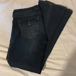 Mörkblå True Religion jeans med kontrastsömmar - Säljer ett par mörkblå jeans från True Religion med ikoniska kontrastsömmar och snygga fickdetaljer. Klassisk femficksmodell med logopatch bak och markerade bakfickor. Jeansen har en rak passform och är tillverkade i robust denim. Använt max 3 gånger Pris kan diskuteras💕
