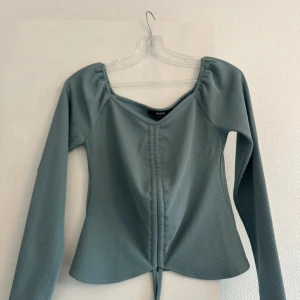 Ljusblå ribbad topp från Bik Bok - Supersnygg ljusblå långärmad topp från Bik Bok i ribbat material. Toppen har en v-ringad hals, snörning framtill och en croppad passform. Perfekt att styla med jeans eller kjol för en trendig look.