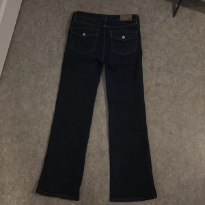 Mörkblå bootcut jeans från 157 - Snygga mörkblå jeans från 157 med klassisk bootcut-passform. Jeansen har raka ben, fem fickor och coola bakfickor med lock och knapp. Materialet är robust denim i bomull och de har en tidlös look som funkar till allt.