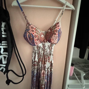 mönstrad klänning - Paisleymönstrad långklänning med smala axelband och smockad midja. Färgerna går i vitt, rött, blått och brunt. Klänningen har en feminin v-ringning och ärmlös design, perfekt för varma dagar. Materialet känns lätt och luftigt. Fråga om bilder på jag skickar då! 💕💕