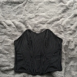 Svart randig korsett från Lindex - Säljer en svart korsett från Lindex med tunna vita ränder. Toppen har klassisk hakknäppning framtill och en snygg formad siluett. Materialet är slätt och känns bekvämt mot huden. Hör av dig för fler bilder eller frågor!