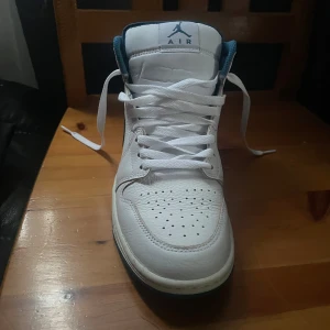 Nike Air Jordan 1 High vit/blå 41 - Säljer ett par Nike Air Jordan 1 High i vitt och marinblått skinn. Klassisk siluett med perforerad tå, snörning och blå detaljer på swoosh, häl och foder. Ikonisk Air Jordan-logga på sidan och Jumpman på plösen. Perfekta för dig som vill sticka ut med stil.