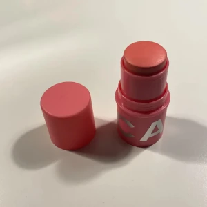 Krämrouge stick från CAIA i berry smoothie - Snygg krämrouge i stickformat från CAIA med en fräsch korallrosa nyans. Förpackningen är rund och kompakt i rosa plast med silvriga bokstäver. Perfekt för att ge kinderna en naturlig glow och lätt att ta med i väskan. Enkel att applicera direkt på huden.