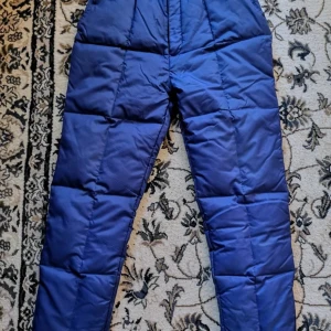 Dunbyxor/Snöbyxor/Täckbyxor med resårmidja Dam - Längd98cm, midja75-85cm innerbenslängd66cm, stl M. Dessa Dunbyxor/Snöbyxor är gjorda av 100% dun, lätt, skön och varm, i jättebra skick. Justerbar resår i midjan och bensluten gör byxan mycket flexibel. Detta är perfekt för vinterbruk med mjuk skal, vindtät och vattentålig kompressionsbyxa för utomhusbruk, naturligtvis kan du också använda den för skidåkning, vintercamping, backpacking, fiske, skidåkning. Tyg: vattentät nylon Foder: mjuk & hudvänlig nylon. Fylling kvalitet dun för att låsa varma