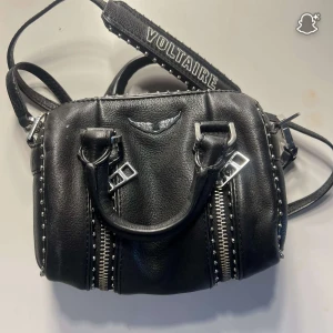 Svart handväska Zadig & Voltaire skinn - Snygg väska från Zadig & Voltaire i skinn med silvriga dragkedjor, nitar och detaljer. Väskan fungerar till allt. Perfekt storlek för det viktigaste och ger en edgy vibe. Den är heller inte så stor så lätt att bära på.