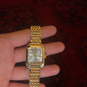 Guldig XIMILI klocka - Snygg klocka från XIMILI med rektangulärt ur i silver och guldig länk. Klockan har en klassisk design med metallarmband och stilren urtavla utan siffror. Perfekt accessoar för dig som gillar en elegant och tidlös look.