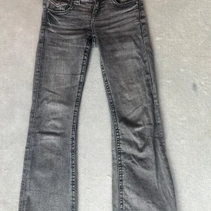 Grå bootcut jeans Gina Tricot - Snygga grå jeans från Gina Tricot i bootcut-modell. Jeansen har klassisk femficksdesign, silverfärgade knappar och cool tvättad look. Perfekta för dig som gillar en avslappnad men trendig stil.
