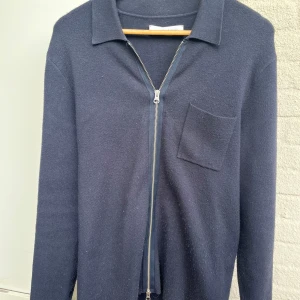 Mörkblå kofta från Samsøe Samsøe - Snygg mörkblå kofta från Samsøe Samsøe med hel dragkedja framtill och en bröstficka. Koftan har klassisk krage och är långärmad, perfekt för lager-på-lager. Materialet är mjukt och stickat, vilket gör den både bekväm och stilren.