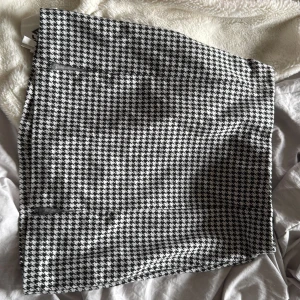 Svartvit rutig kortkjol från Divided - Snygg svartvit kortkjol från Divided med klassiskt hundtandsmönster. Kjolen har en rak passform och är tillverkad i ett mjukt polyestermaterial. Perfekt för dig som gillar stilrena och trendiga plagg med lite edge.