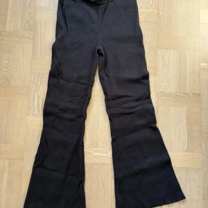 Svarta ribbade byxor  - Svarta ribbade byxor från Tommy Jeans i storlek M. Byxorna har bootcut-ben och en bakficka med Tommy Jeans-logga. Mjukt och stretchigt material.