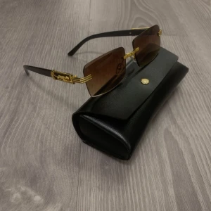 Svarta solglasögon med gulddetaljer -  Riktigt snygga solglasögon med rektangulära, bruna glas och svarta skalmar. Guldiga detaljer med leopard på sidorna. ALDRIG ANVÄNDRA, TILLBEHÖR INGÅR