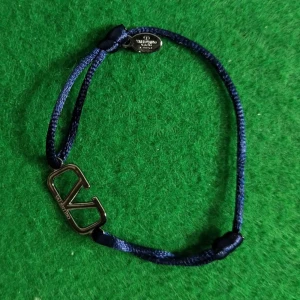 Valentino blått armband med logga - Snyggt armband från Valentino med justerbart blått band och en metallfärgad logga i mitten. Perfekt accessoar för att lyfta din outfit med en stilren touch och exklusiv känsla. Bandet är i textil och loggan har en cool, minimalistisk design.