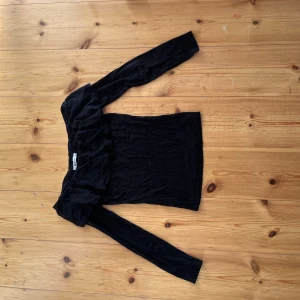 Svart offshoulder topp Gina Tricot - Svart offshoulder topp från Gina Tricot i storlek XS. Toppen har långa ärmar och en snygg volangdetalj längs axlarna som ger en cool och trendig look. Perfekt att styla med jeans eller kjol för en stilren outfit.