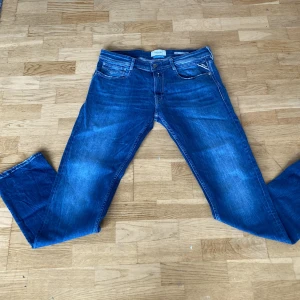 Blå Replay jeans straight fit - Snygga blå jeans från Replay med klassisk femficksdesign och raka ben. Jeansen har tydliga slitningar och kontrastsömmar, samt Replay-logga vid fickan. Materialet är robust denim och modellen är straight fit, perfekt för en chill och stilren look.Helt nya oanvända